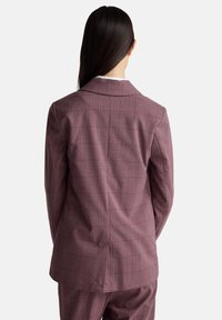 Blazer a quadri bordeaux con una vestibilità su misura, caratterizzato da un rever a V e un'apertura centrale sul retro. Realizzato in tessuto testurizzato.
