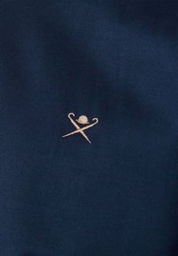 Małe beżowe wyszywane logo kapelusza melonik z skrzyżowaną parasolką i laską na ciemnoniebieskim tle materiału.