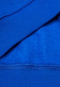 Tessuto blu con una finitura liscia e texturizzata. Presenta un orlo rigato e cuciture con un filo di colore contrastante. Strati visibili.