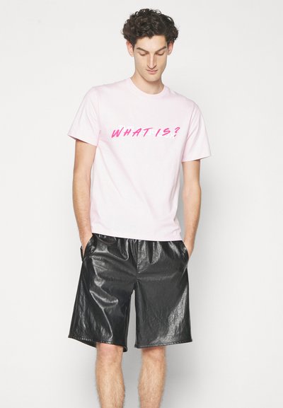 Rosa bomull T-skjorte med teksten "HVAD ER?" i kontrastfarge rosa, kombinert med svarte glitrende faux skinnshorts med sidelommer.