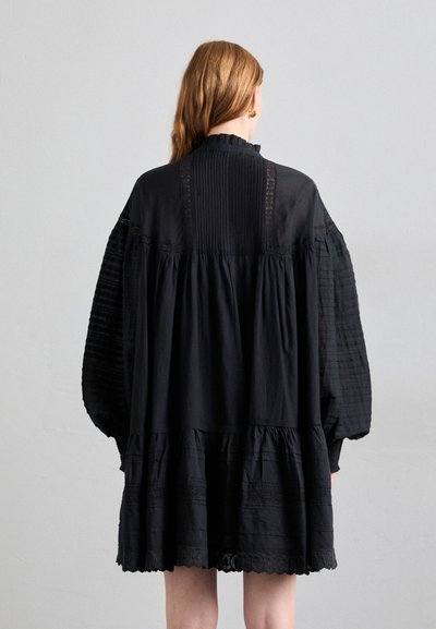 Zwarte jurk met een gelaagd ontwerp, heeft geplooide stof op de mouwen, een hoge kraag en kanten details langs het lijfje.
