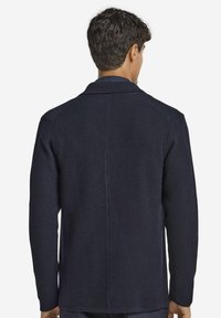 Marineblå strikket cardigan med en struktureret overflade, skrå krave og en midterseam bagpå. Lange ærmer og lige snit.