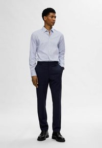Camicia a righe azzurro chiaro con bottoni abbinata a pantaloni blu scuro e scarpe nere. Il materiale sembra liscio; la camicia ha un colletto classico e polsini.
