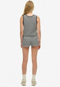 Gestreepte tanktop en shortset in zwart en wit. Zachte stof, mouwloos ontwerp. Accesoires omvatten witte sokken en lichtgekleurde sneakers.