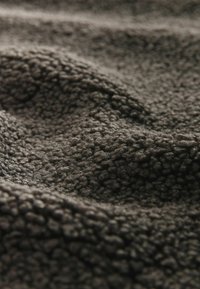 Tamsiai pilka tekstūruota medžiaga su minkštu, pūkuotu paviršiumi, su banguota struktūra ir puriu išvaizda, tinkanti šilumai ir komfortui.