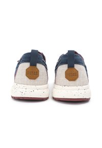 Zapatillas azules y beige con un upper de tela texturizada, parche de logo y suela blanca moteada. Presentan una pestaña en la parte posterior para facilitar el uso.