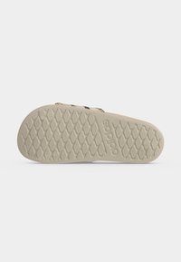 Σόλα από μπεζ σανδάλι Adidas slide με ανάγλυφο μοτίβο κράτησης και σήμα Adidas σε απλό λευκό φόντο.