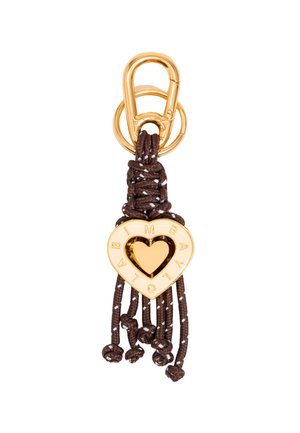 Gold heart-shaped charm with cutout center and engraved letters, attached to brown braided cord and loop, featuring tassel ends and beads.