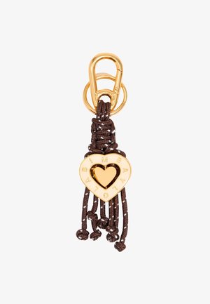 Charm en forme de cœur en or avec un centre découpé et des lettres gravées, fixé à un cordon tressé brun et une boucle, avec des extrémités à franges et des perles.