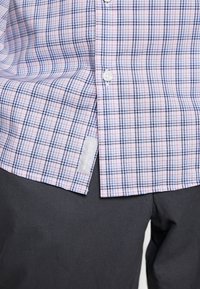 Camicia a maniche corte con bottoni in un motivo a quadri rosa e blu, dotata di un'etichetta sul lato sinistro inferiore e bottoni bianchi. Abbinata a pantaloni scuri.