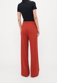 Breda byxor i rostorange tyg med en mjuk textur, hög midja och bakfickor. Stylande med en åtsittande svart topp.