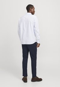Hellblaues Button-Down-Hemd mit langen Ärmeln, kombiniert mit marineblauen maßgeschneiderten Hosen und braunen Schuhen, von hinten betrachtet.