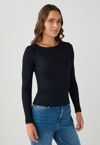 Schwarzes, geripptes Langarmshirt mit Rundhalsausschnitt, figurbetontem Schnitt und glatter Textur, kombiniert mit blauen High-Waist-Jeans.