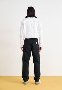 Black cargo pants with multiple pockets, worn with a white striped button-up shirt. The shirt has a relaxed fit and visible stitching.