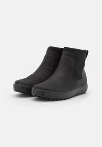 Botine negre până la gleznă, fabricate dintr-un suede moale cu un finisaj neted, având panouri elastice laterale, o talpă groasă cu striații și un fel de ureche în spate.
