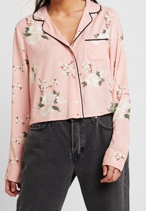 Lyserød langærmet skjorte med knapper, prydet med blomsterprint og sort pyntestribe, båret med højttaljede, falmede sorte jeans.