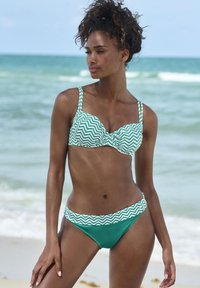 Costume da bagno a righe zigzag verde e bianco con coppa imbottita e slip a vita bassa. Tessuto liscio con banda a contrasto in vita.
