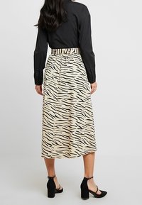 Midi sukně v béžové barvě s černými tygřími pruhy, s elastickým pasem a volným střihem. Spárována s černými lodičkami na kotníče.
