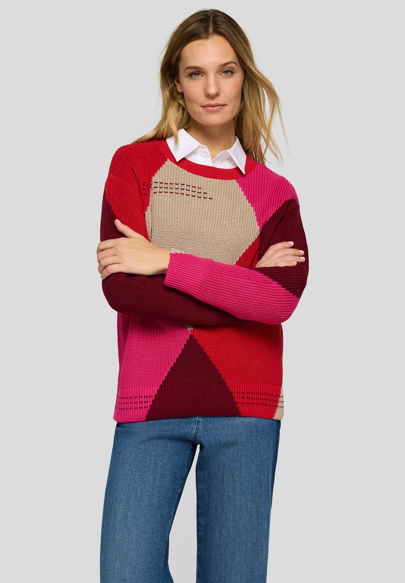 Gestrickter Pullover mit geometrischen Mustern in Rot, Rosa und Beige. Rundhalsausschnitt mit strukturierten Details, getragen über blauen Jeans.
