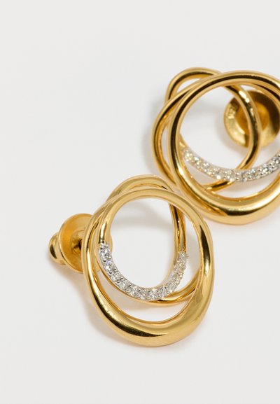 Guld hoops øreringe med sammenflettede cirkulære designs, prydet med en række klare, funkende ædelstene på den ene side. Glat tekstur.