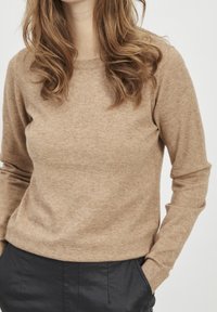 Beige knitted sweater with long sleeves and a round neckline. Soft texture, fitted design, paired with dark trousers.