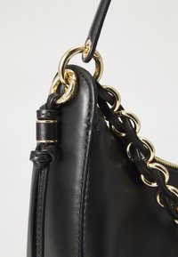 Borsa a mano in pelle nera con un design strutturato, dettagli in catena color oro e una tracolla intrecciata. Texture liscia con cuciture visibili.