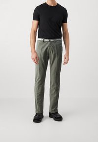 Pantalon vert en coton à coupe slim, avec une ceinture blanche. Associé à un t-shirt noir à manches courtes et des baskets noires.