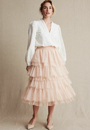 Vit blus med blomsterbroderier, puffärmar och djup V-ringning, matchad med en lager av rosa tyllkjol. Platta ljusa skor fulländar looken.