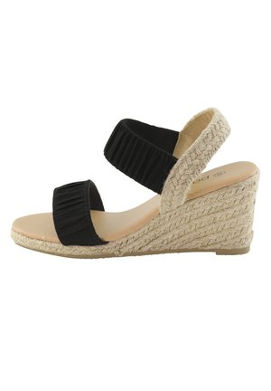 Kile-sandal med beige flettet rebssål og to sorte elastiske stropper over fod og ankel.