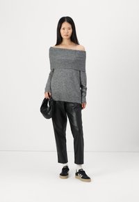 Pull gris décolleté avec texture côtelée, associé à un pantalon en faux cuir noir. Baskets noires avec semelles crème et sac noir.