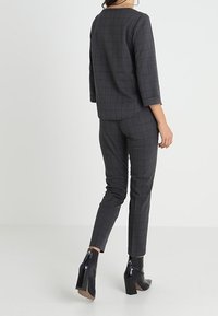 Top e pantaloni aderenti a quadri grigi realizzati in tessuto testurizzato, abbinati a stivaletti neri con tacco alto, visti da dietro.