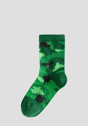 Chaussette en coton vert avec un motif camouflage, présentant des nuances variées de vert et des accents éclaboussés de noir. Haut côtelé pour plus d'élasticité.