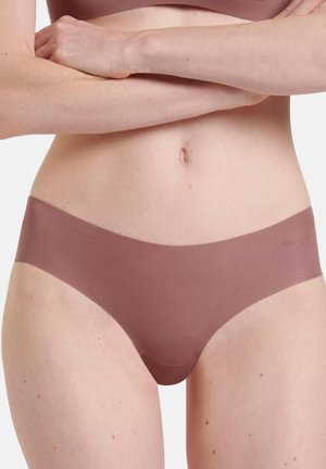 Woman wearing mauve seamless hipster underwear, arms crossed above waist, against a plain light background.