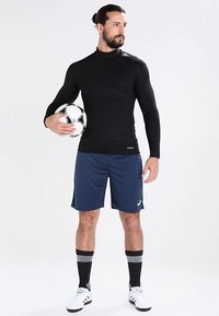 Μαύρο αθλητικό μπλουζάκι με μακριά μανίκια, μπλε σορτς, μαύρες κάλτσες μέχρι το γόνατο, κρατώντας μια μπάλα ποδοσφαίρου. Διαθέτει υφή σχεδίασης και λογότυπο.