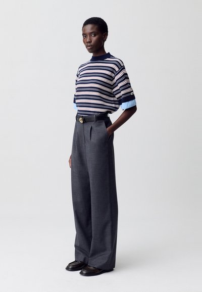 Top de punto de manga corta a rayas en color marino, crema y azul claro; pantalones grises de cintura alta con pliegues; estilizado con un cinturón negro y zapatos planos.