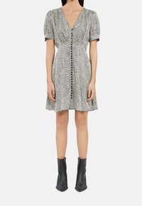 Sukienka w panterkę w czerni i bieli z bufkowymi rękawami, dekoltem w serek i detalami na guziki z przodu, zestawiona z czarnymi botkami za kostkę.