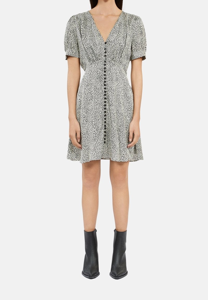 Sukienka w panterkę w czerni i bieli z bufkowymi rękawami, dekoltem w serek i detalami na guziki z przodu, zestawiona z czarnymi botkami za kostkę.