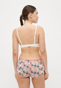 Fehér párnázott bralette állítható pántokkal, multiszínű geometriai mintás rövidnadrággal párosítva, narancssárga derékkal.