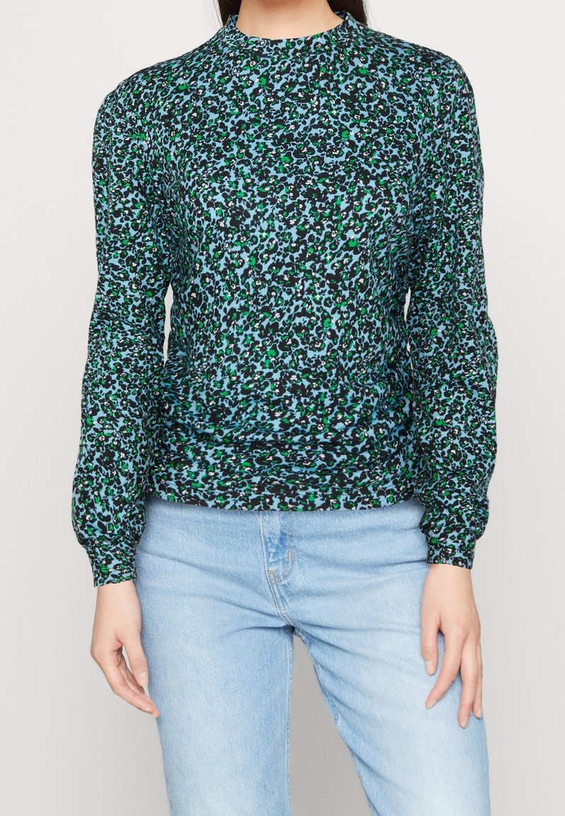 Svart långärmad topp med ett grönt och blått abstrakt djurmönster, hög hals och rynkade detaljer vid fållen. Bärs med ljusblå jeans.