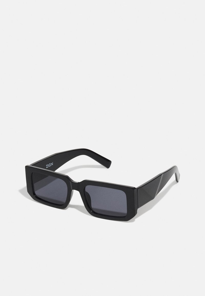 Óculos de sol retangulares pretos com armações grossas e lentes escuras. Projetados com bordas angulares e um logotipo discreto na haste.