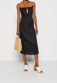 Svart linn midi-klänning med en nyckelhålsdetalj fram och tunna axelband, tillsammans med en vävd halm-väska och krämfärgade öppna klackskor med blockklack.
