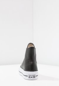 Svart lær høye sneakers med hvit gummisåle, med et rundt logo-merke på den ytre siden og kontrasterende søm.