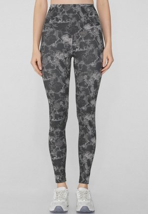 Leggings negros con un patrón abstracto gris texturizado, material elástico, cintura alta y un silueta ajustada, combinados con zapatillas blancas.