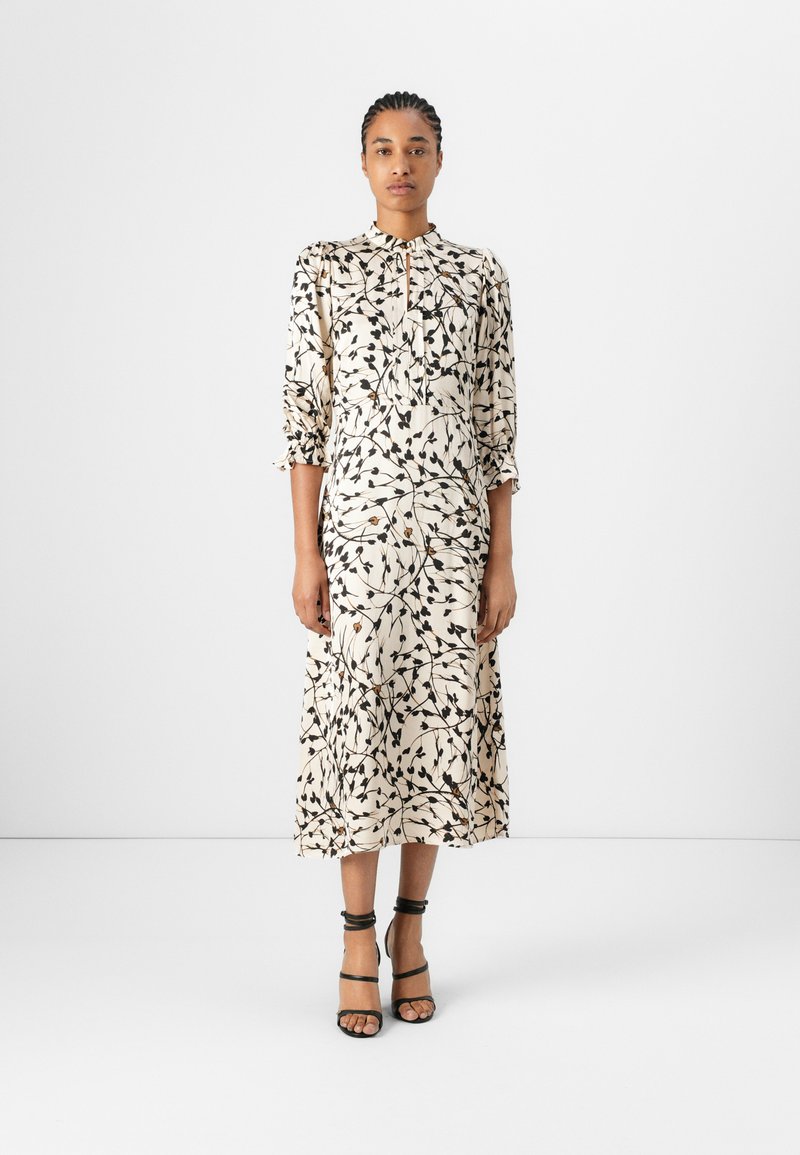 Maxikleid aus cremefarbigem Stoff mit schwarzen botanischen Mustern. Es hat einen Kragen, eine durchgehende Knopfleiste und halblange Ärmel. Der Saum ist fließend.