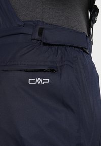 Gros plan sur un pantalon imperméable bleu marine avec ceinture ajustable, poche zippée et logo CMP sur la hanche.