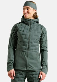 Green insulated jacket with a quilted front, zipper closure, and hood. Softshell sides, thumbholes, and logo detail on the lower right.