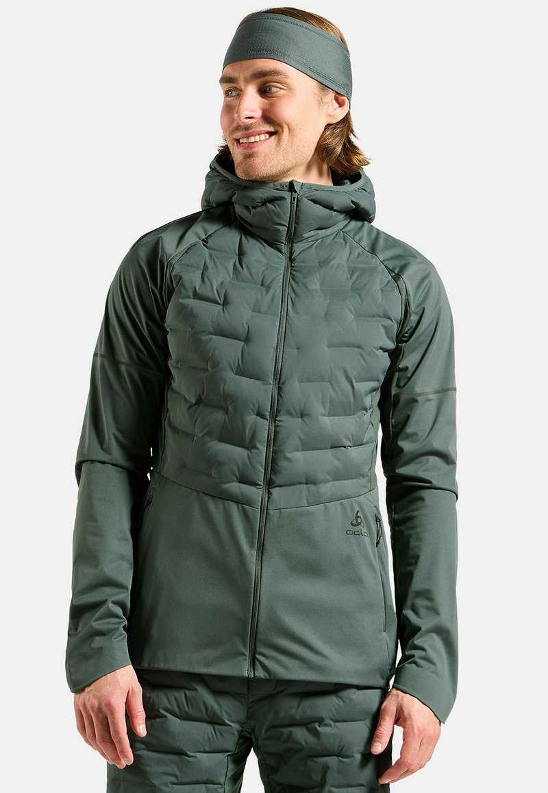 Green insulated jacket with a quilted front, zipper closure, and hood. Softshell sides, thumbholes, and logo detail on the lower right.