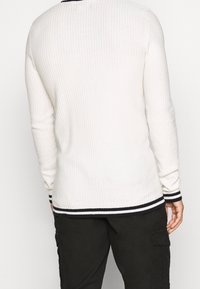 Bílé žebrované svetr s dlouhými rukávy, námořnicky pruhovaný lem u krku a manžety, s úzkým střihem a texturou pro zvýšené teplo a styl.