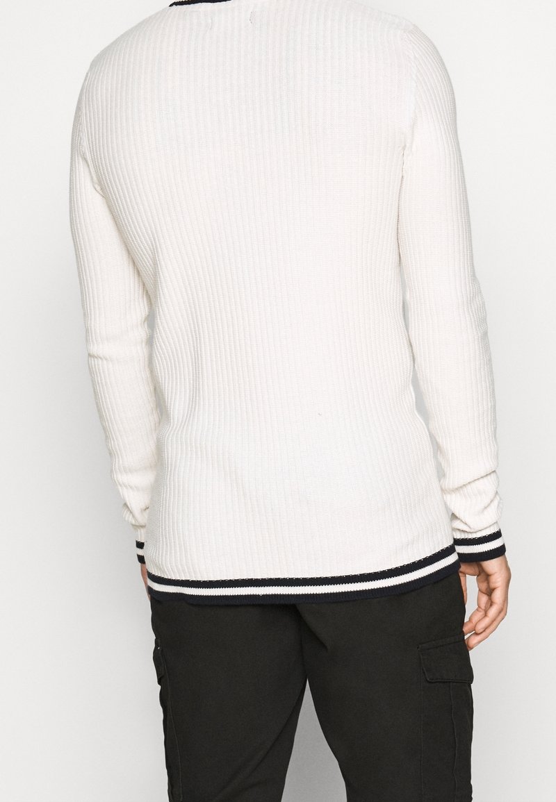 Bílé žebrované svetr s dlouhými rukávy, námořnicky pruhovaný lem u krku a manžety, s úzkým střihem a texturou pro zvýšené teplo a styl.