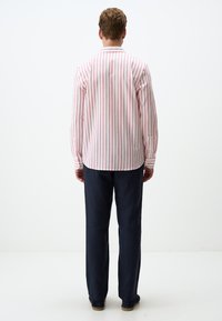 Chemise à manches longues pour homme avec des rayures verticales blanches et rouges, associée à un pantalon bleu marine foncé. Poignets à boutons et détail d'ourlet droit.